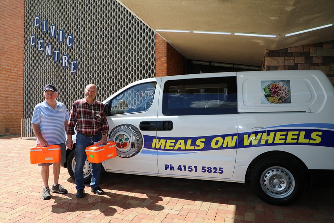 Volontärer från Meals on Wheels står vid sin skåpbil, redo att leverera måltider.
